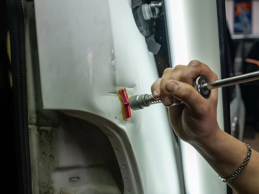 Technician using specialized tools for paintless dent repair on a vehicle panel